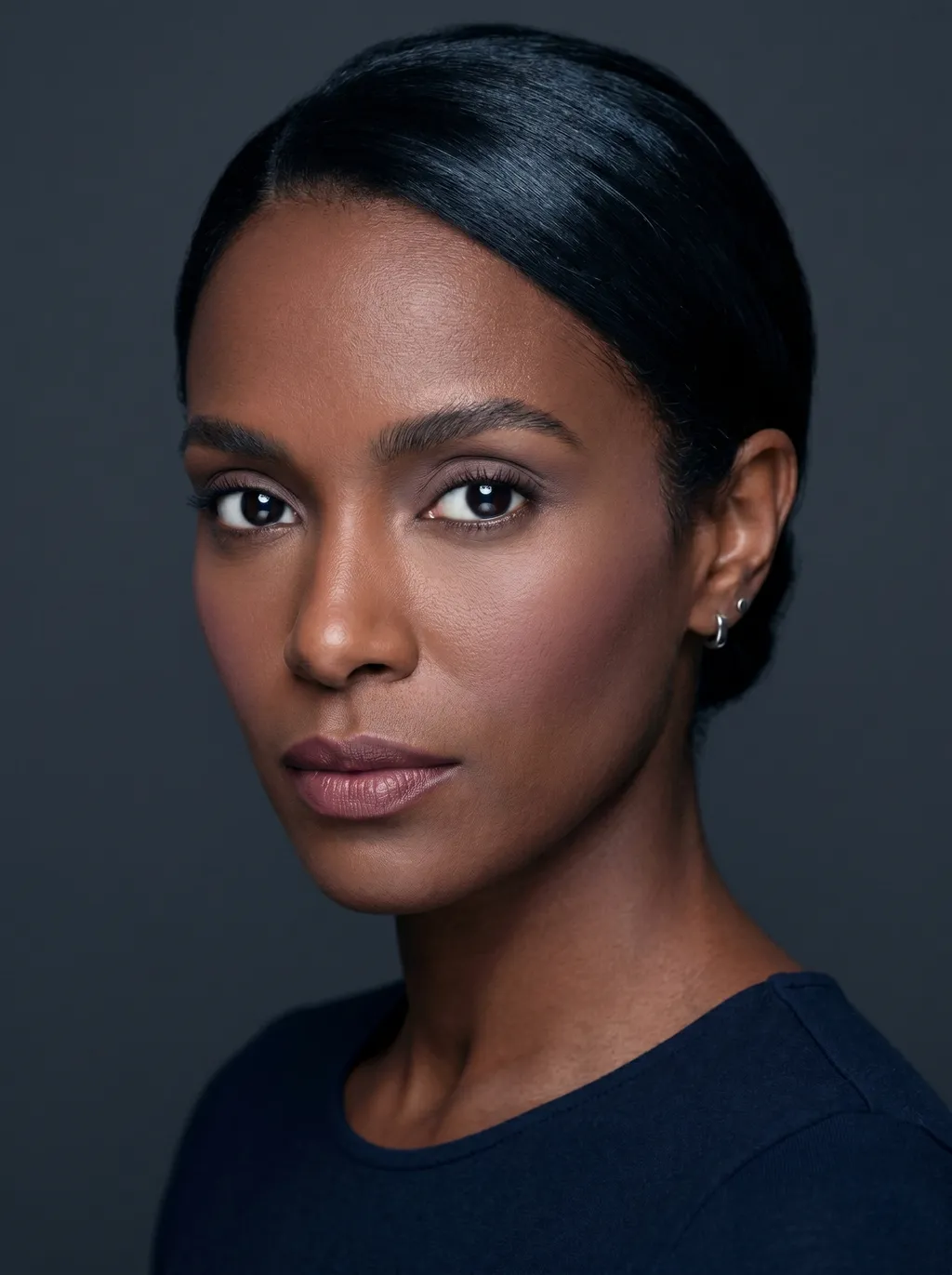 Dark Winter clean girl makeup on deep cool-toned skin: sheer cool taupe lids, soft blush, groomed brows, and a cool mauve-nude lip with sleekly pulled-back hair against a charcoal background