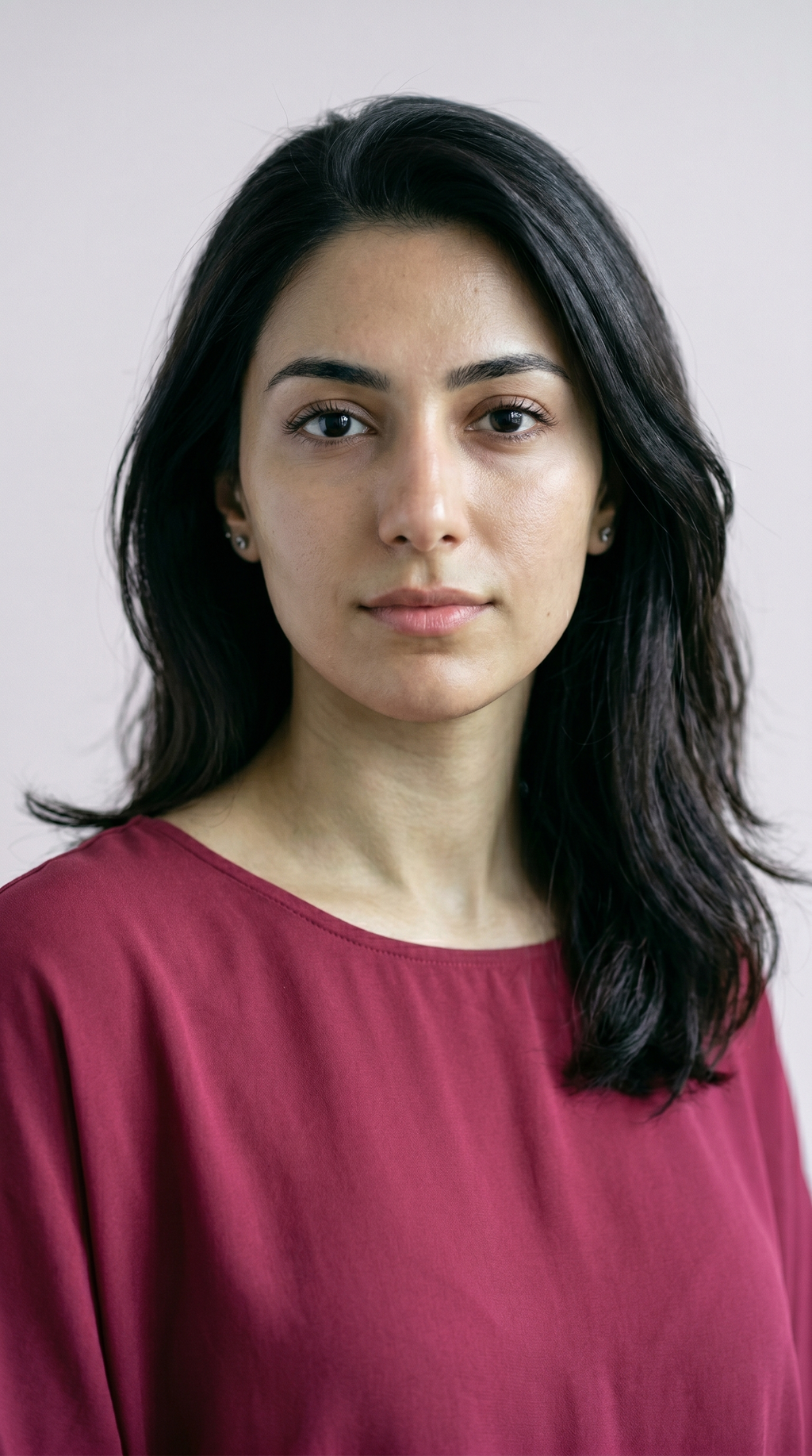 Bare-faced portrait of a woman with cool olive skin, a green-gray cast over a pink-based undertone, dark hair, against a soft gray background